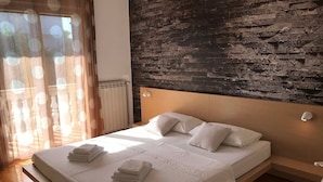 Une chambre moderne avec une tête de lit en bois, un grand lit recouvert de linge de maison blanc et un mur décoratif à motifs de briques.