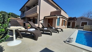 Un bâtiment à deux étages doté d’une piscine, de chaises longues et d’une table sur laquelle se trouvent un chapeau et une serviette.