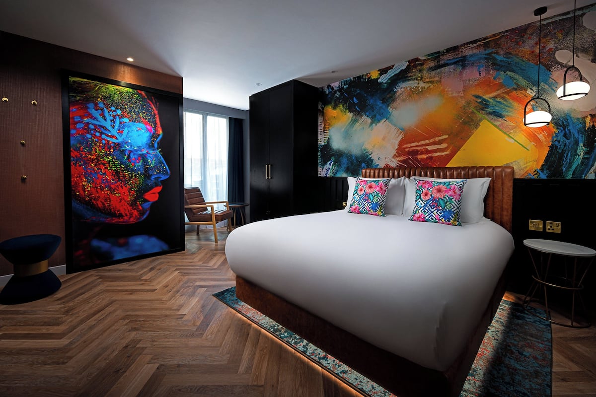 Une chambre moderne avec un grand lit, une peinture abstraite aux couleurs vives et un parquet en bois disposé en chevrons.