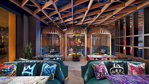 A modern interior with green leather seating, wooden beams, and colorful artwork. - NYX Hotel Dublin Portobello (Dublin)