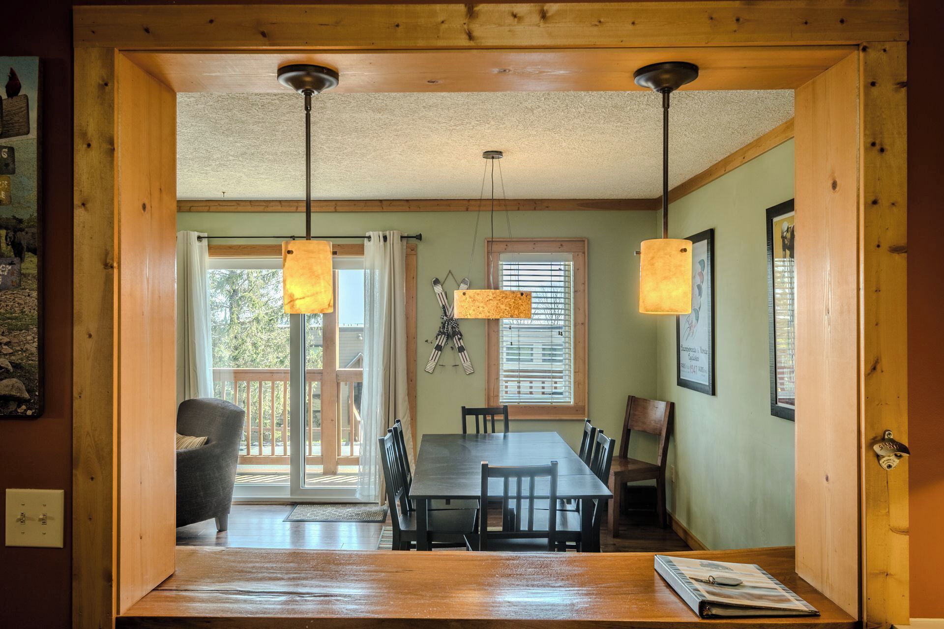 A dining area with a wooden table and chairs, a hanging light fixture, and a window with blinds.