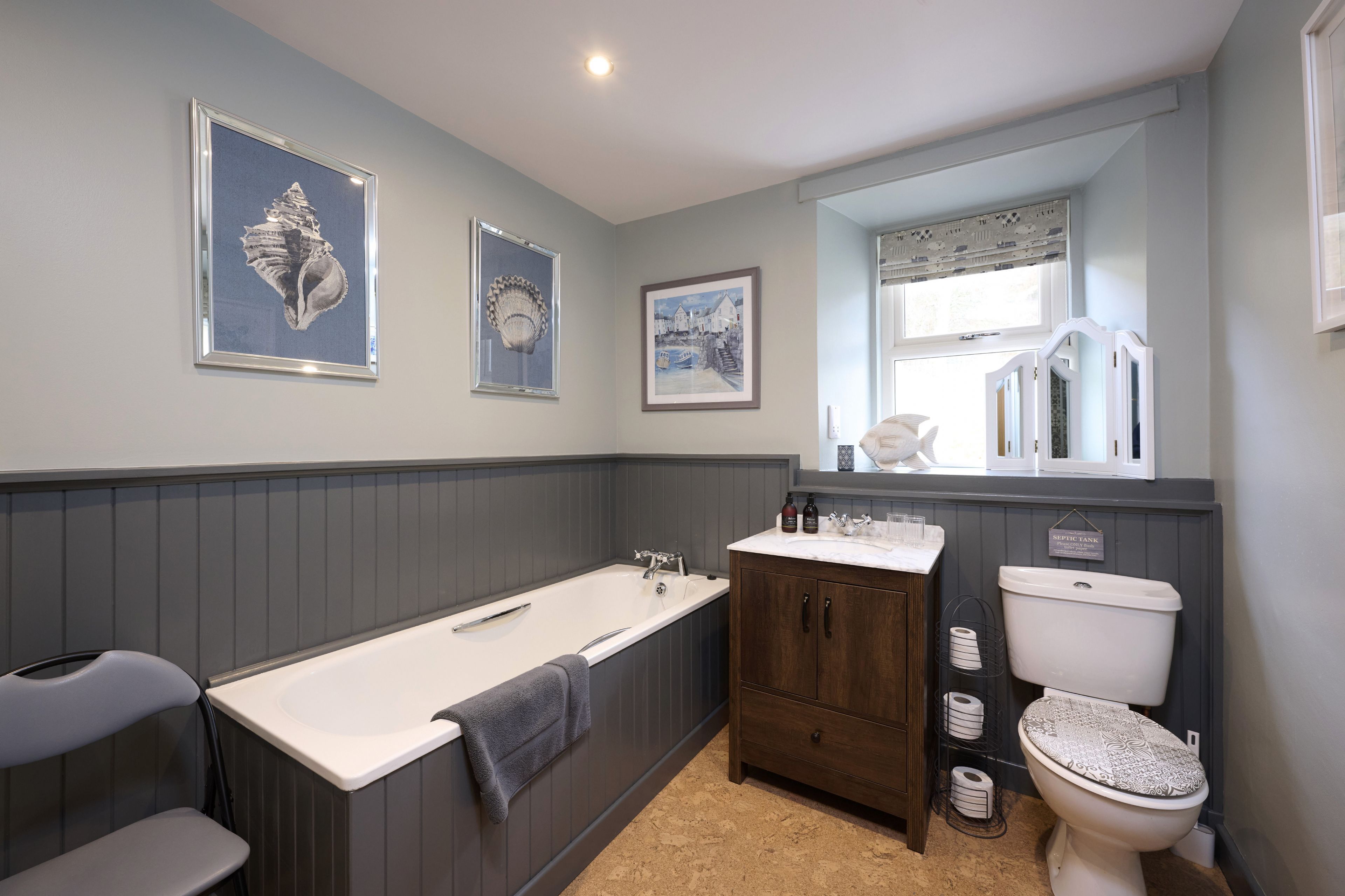 A bathroom with a bathtub, vanity, and toilet. There are framed pictures on the wall and a window above the toilet.