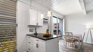Una cocina moderna con armarios blancos, una encimera negra y un comedor con sillas y mesa de madera.