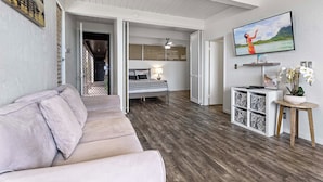 Una sala moderna con un sofá, un televisor en la pared y una cama al fondo.
