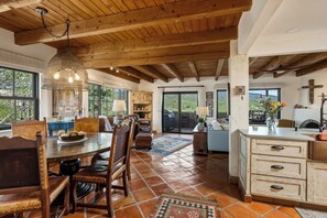A rustic interior with a wooden ceiling, a dining area with a table and chairs, and a kitchen with a sink and cabinets.