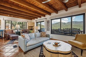A spacious living room with a high ceiling, large windows, and a view of a mountainous landscape.