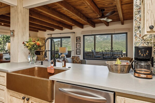 A kitchen with a stainless steel sink, a coffee maker, and a view of the outdoors.