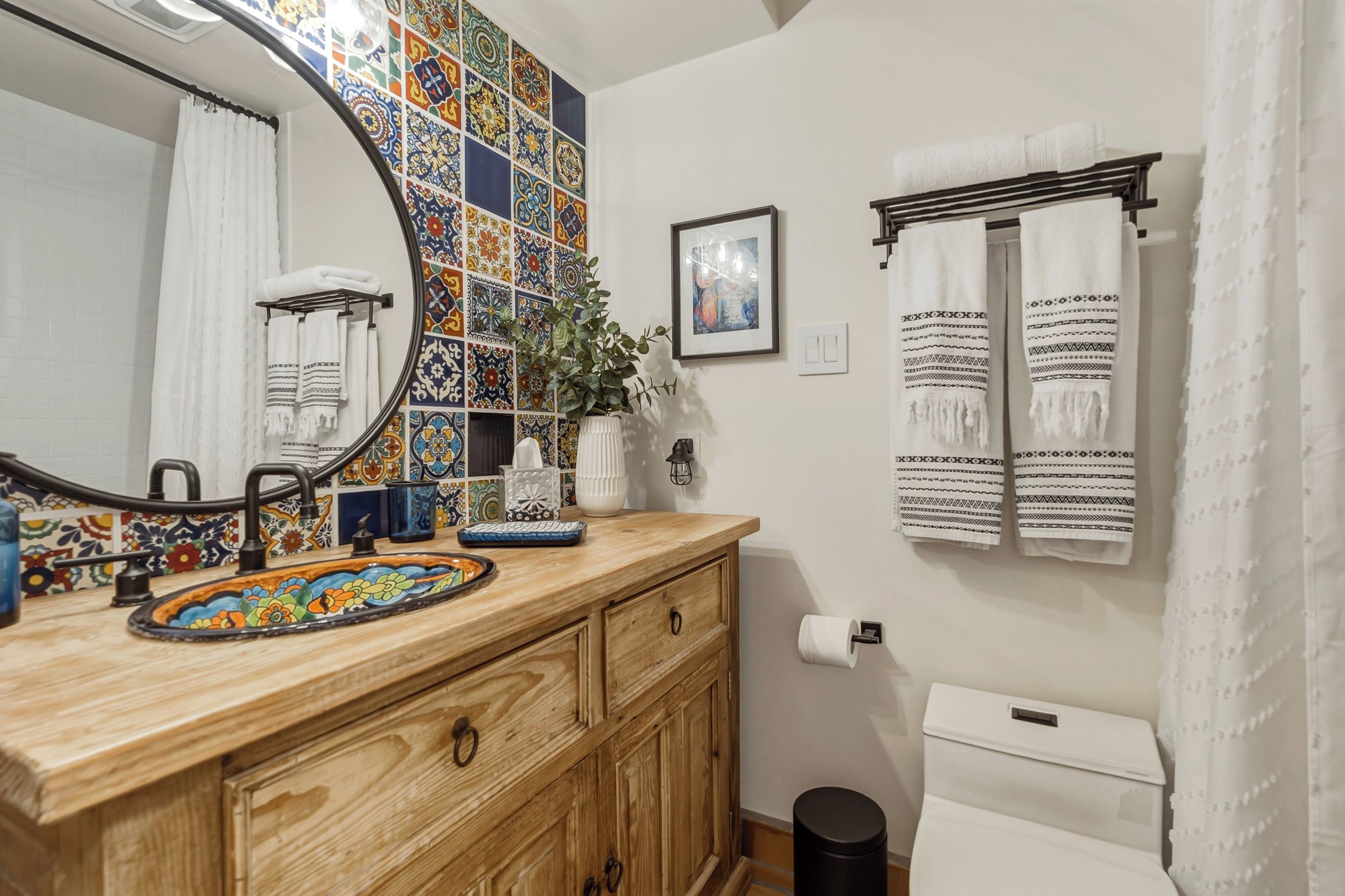 A bathroom with a wooden vanity, a colorful tiled backsplash, a large mirror, and a toilet with a white tank.