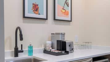 Una cocina moderna con un lavamanos de acero inoxidable, una cafetera y un tostador. Hay dos cuadros enmarcados en la pared sobre la encimera.