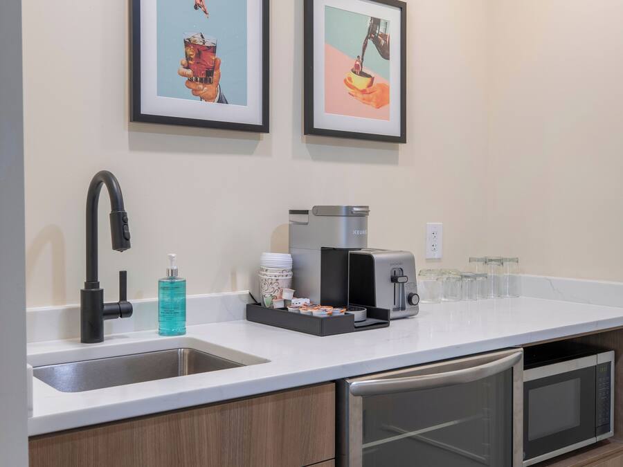 Una cocina moderna con un lavamanos de acero inoxidable, una cafetera y un tostador. Hay dos cuadros enmarcados en la pared sobre la encimera.