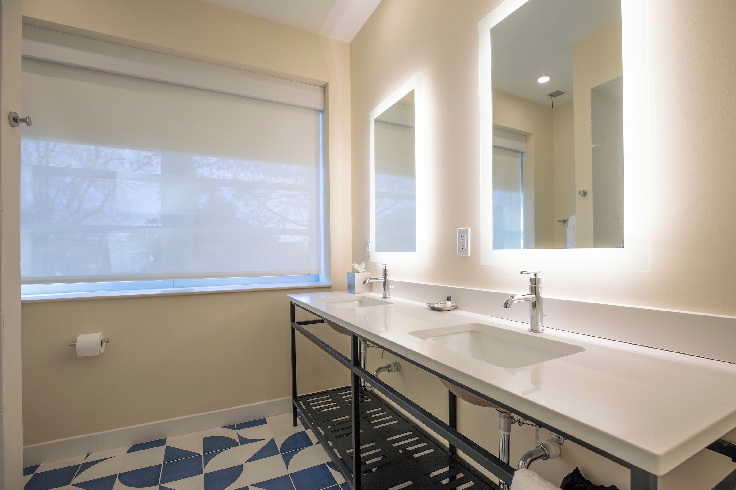 Een moderne badkamer met twee wasbakken, een grote spiegel en een raam met zonwering.