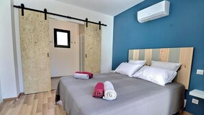 Ein Schlafzimmer mit einem Bett, zwei Kissen, einem Fenster, einer Klimaanlage und einer mit Vorhang versehenen Tür.