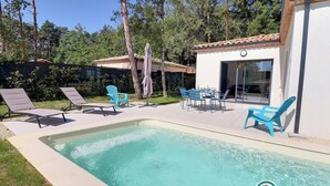 Ein Swimmingpool mit Liegestühlen und einem Tisch, umgeben von Bäumen und einem Gebäude mit einem Ziegeldach.