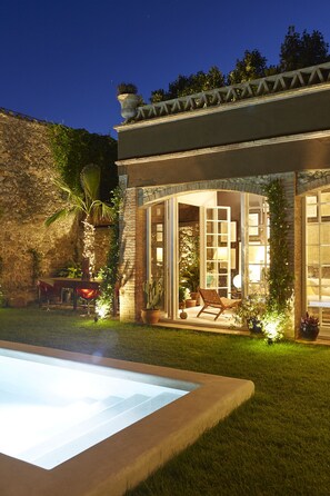 A well-lit patio area with a pool, stone walls, and outdoor seating. - llimona suites (Corca)