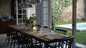 Une table à manger, avec des chaises, une bougie et des verres à vin, donnant sur un jardin et un mur de pierre en arrière-plan.