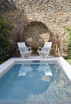 A swimming pool with two white lounge chairs and a stone wall in the background. - llimona suites (Corca)