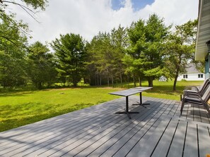 A deck with a table and chairs, surrounded by trees and a grassy lawn, with a house in the background.