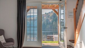 Ein Schlafzimmer mit einer großen Schiebeglas-Tür, die auf einen Balkon mit Blick auf einen See und Hügel führt.