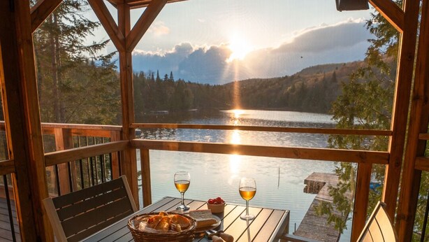 Eine Holzterrasse mit Tisch und Stühlen, mit Blick auf einen See bei Sonnenuntergang.