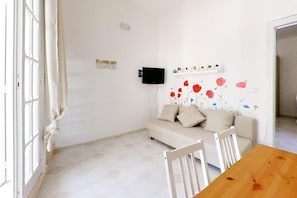 A room with a sofa, a TV mounted on the wall, a wooden table, and a window with curtains.