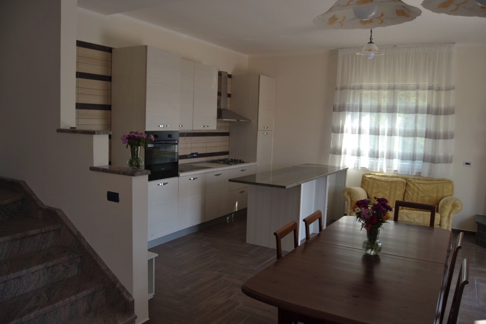 A modern kitchen with white cabinets, a central island, and a dining area with a wooden table and chairs.