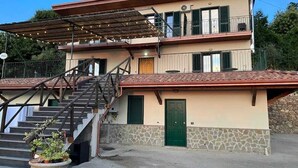A two-story building with a staircase, a covered outdoor area, and a green door. - 20 min from Pompeii and 35 min from Amalfi, structure surrounded by greenery (Campania)