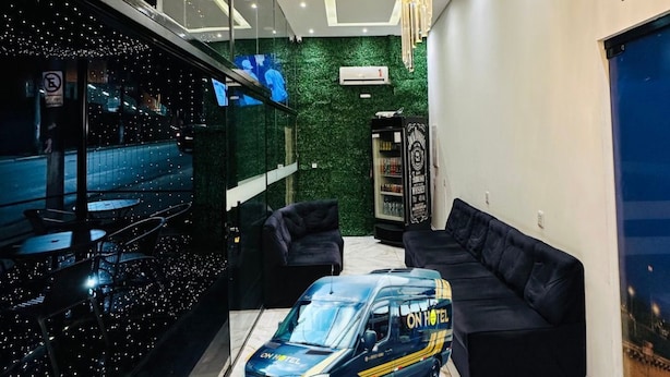 A modern hotel lobby with a glass wall, a chandelier, a black sofa, and a Mercedes van. - On Hostel gru unidade 2 traslado café  (Guarulhos)