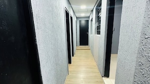 A corridor with grey walls, wooden flooring, and multiple doorways leading to rooms. - On Hostel gru unidade 2 traslado café  (Guarulhos)