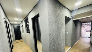 A hallway with concrete walls, wooden flooring, and multiple doorways leading to rooms. - On Hostel gru unidade 2 traslado café  (Guarulhos)