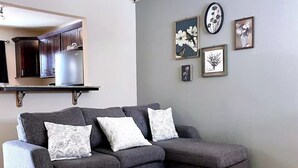 A modern living room with a grey sectional sofa, a round rug, and a kitchen area visible through an open door. - Alaska Townhouse Getaway: Anchorage Cozy Retreat - Close to Downtown (Anchorage)