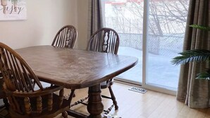 A dining area with a wooden table and chairs, a hanging light fixture, and a large window with curtains. - Alaska Townhouse Getaway: Anchorage Cozy Retreat - Close to Downtown (Anchorage)