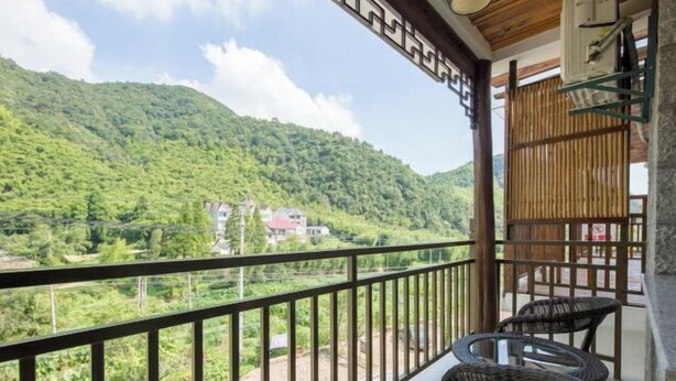 A balcony with wicker chairs, a view of a green mountain, and a building in the distance. - Ziyan Shanju Inn (Deqing)