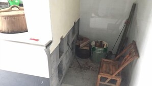 A narrow, dimly lit corridor with a wooden chair, a green bucket, and a black container. - Ziyan Shanju Inn (Deqing)