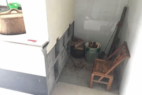 A narrow, dimly lit corridor with a wooden chair, a green bucket, and a black container. - Ziyan Shanju Inn (Deqing)