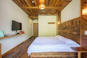 A bedroom with a wooden ceiling, a bed with white bedding, a television on a shelf, and a wooden wall panel. - Ziyan Shanju Inn (Deqing)
