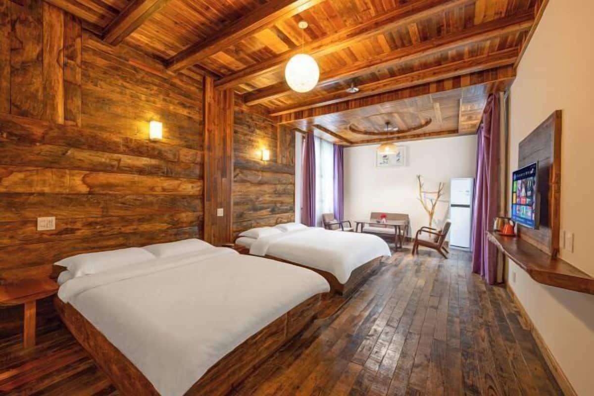 A room with wooden walls and floors, two beds, a small table, and a TV.