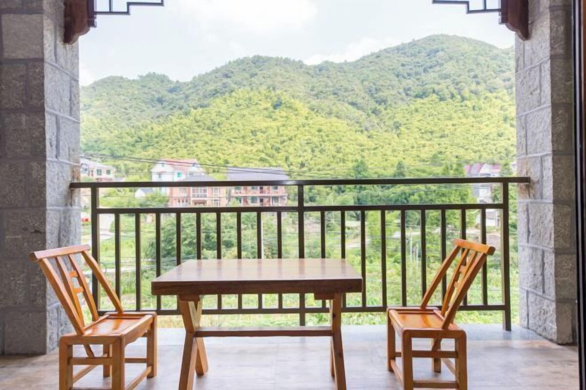A balcony with a wooden table and two chairs, overlooking a mountainous landscape.
