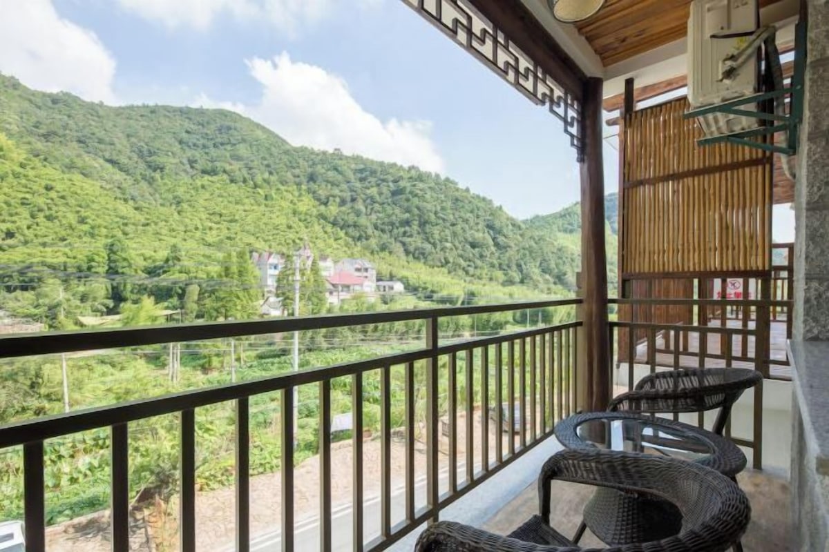 A balcony with wicker chairs, a view of a green mountain, and a building in the distance.