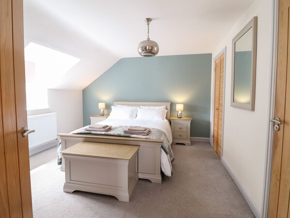 A bedroom with a bed, bedside tables, a hanging light fixture, a wooden bench, and a window.