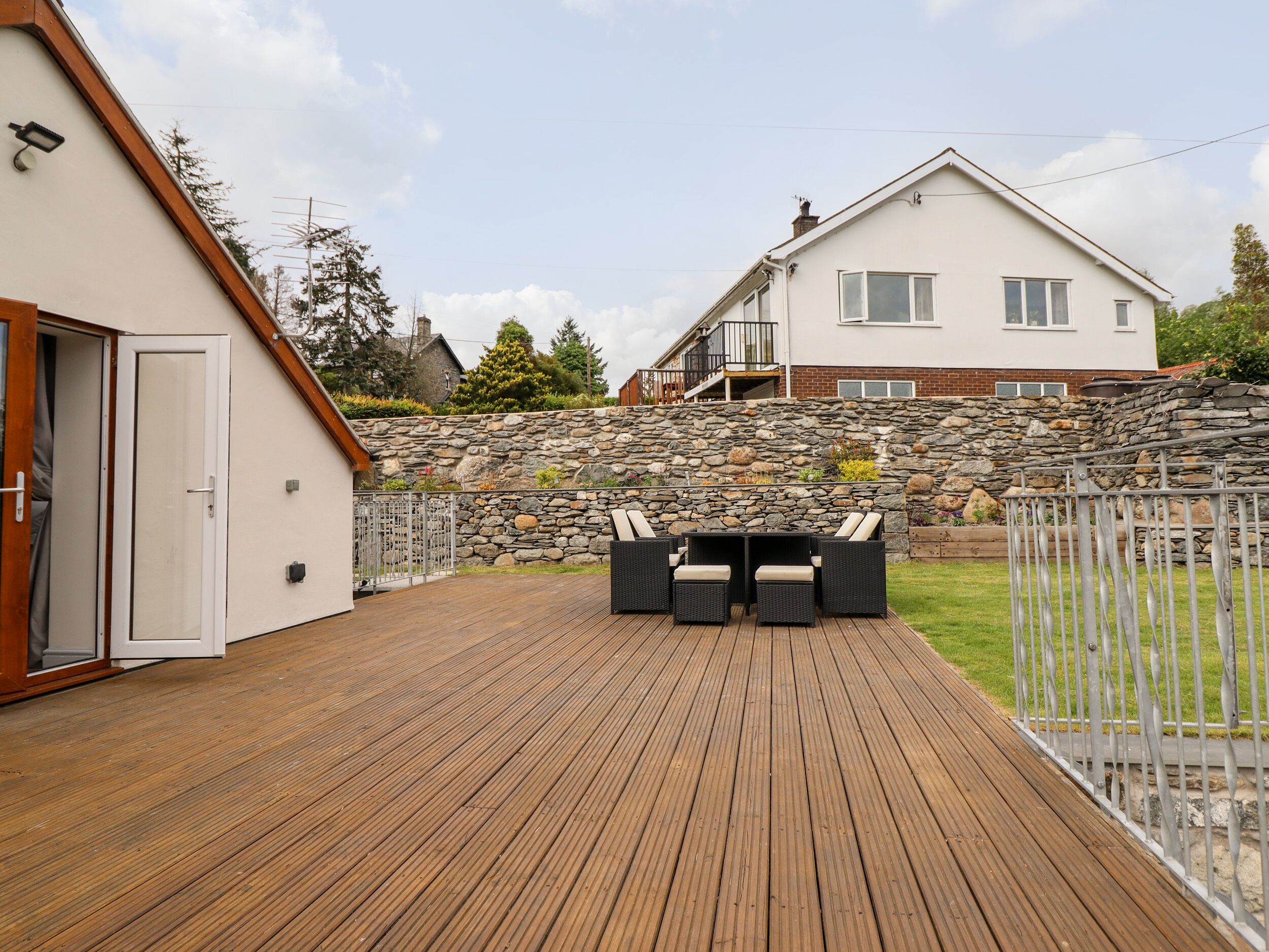 Une terrasse en bois avec des meubles d’extérieur, un mur en pierre et une maison blanche dotée d’un balcon.