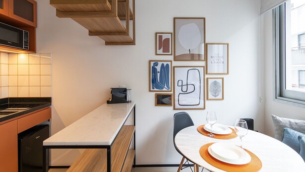 A modern kitchen with a built-in microwave, a dining area with a white table and orange placemats, and a staircase. - VN Frei Caneca (São Paulo)