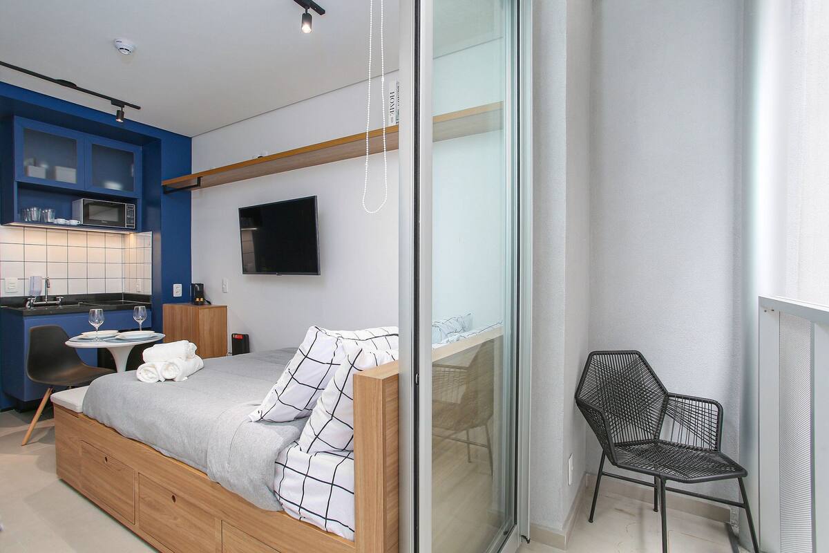 A modern hotel room with a bed, a small kitchenette, a dining area, and a seating space.