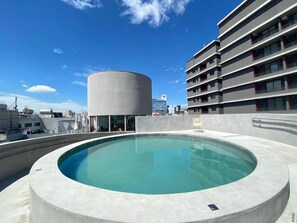 Una piscina en la azotea con diseño circular, rodeada de edificios modernos y un cielo despejado.