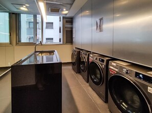 A laundry area with a black sink, three stacked washing machines, and a stainless steel wall. - VN Frei Caneca (São Paulo)