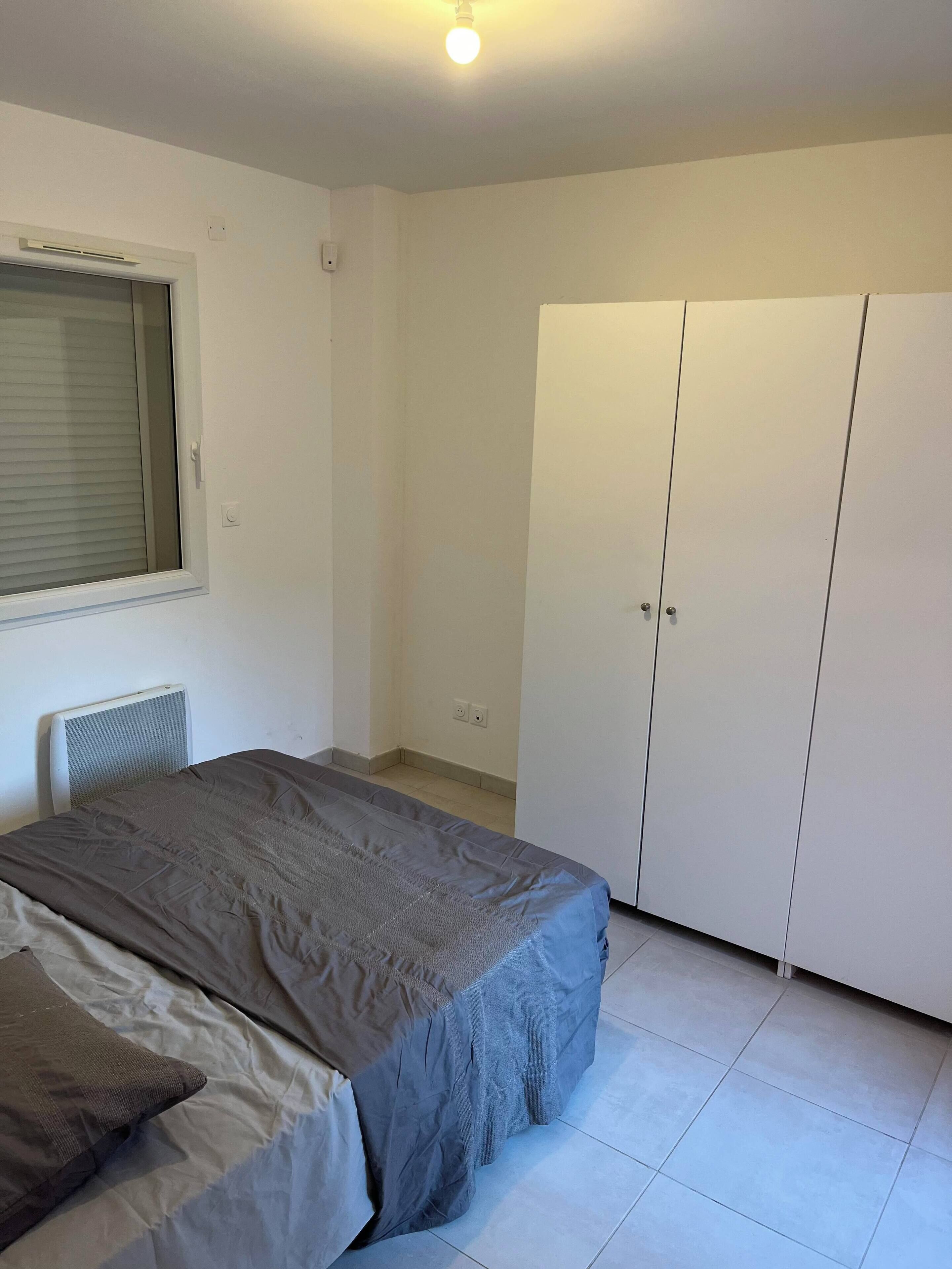 Une chambre à coucher comprenant un lit, une armoire, une fenêtre avec des stores et un luminaire au plafond.