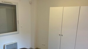 Et soveværelse med seng, garderobeskab, et vindue med rullegardiner og en loftlampe.