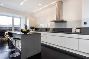 Una cocina moderna con una isla central, armarios blancos y electrodomésticos de acero inoxidable.