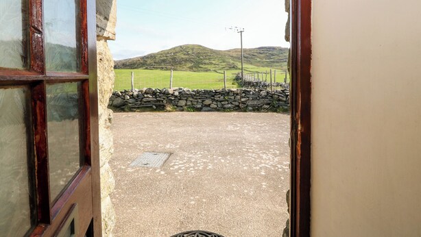 A view through a doorway to a stone wall and a grassy field with a hill in the background. - Ereiniog (Garndolbenmaen)