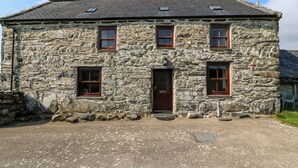 A stone building with a central door, two windows on each side, and a small porch area. - Ereiniog (Garndolbenmaen)