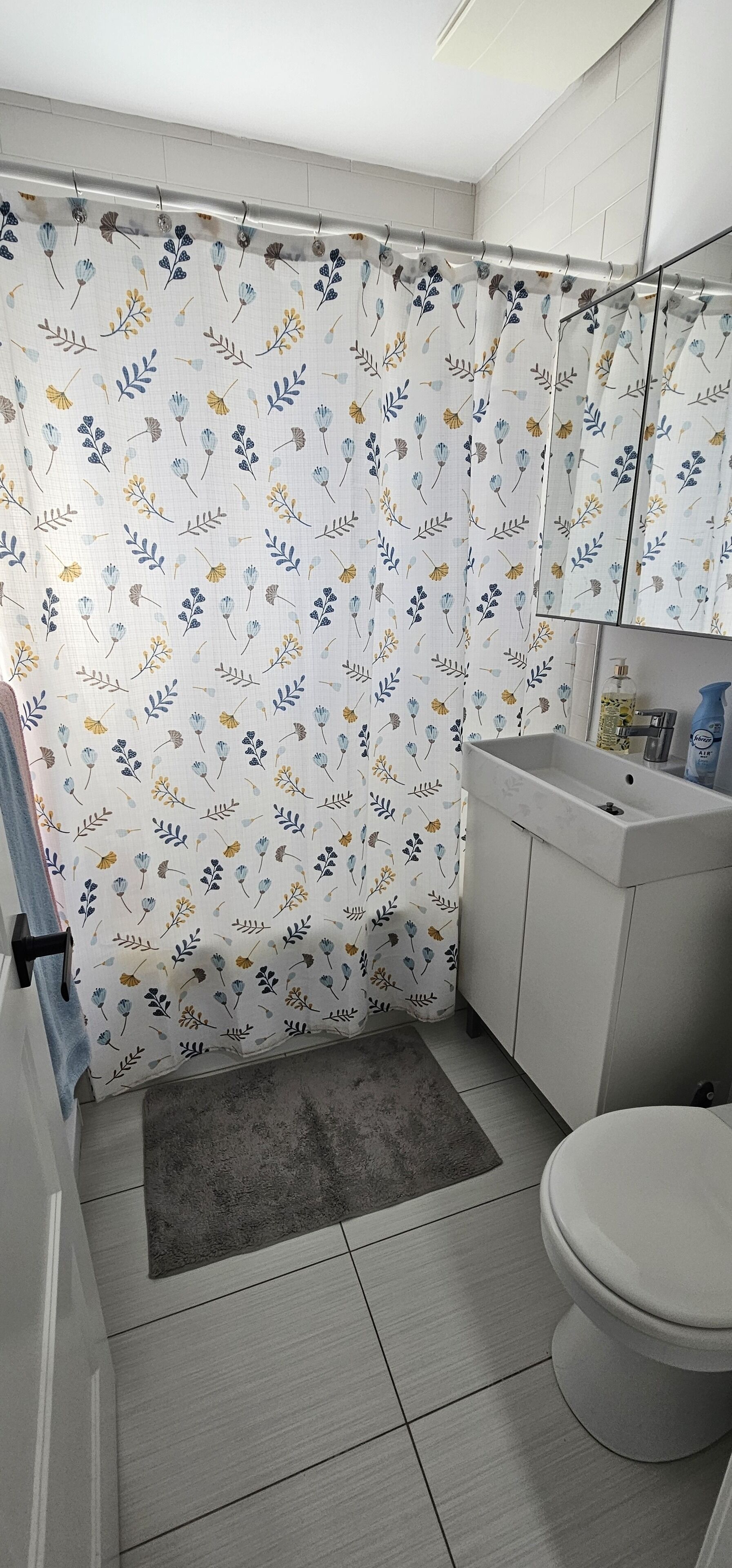 A bathroom with a shower curtain featuring a floral pattern, a white sink, a mirror above the sink, and a toilet.